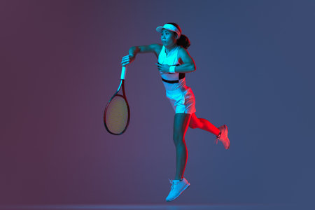 Studio shot of active professional tennis player training with tennis racket over gradient pink-purple background in neon light. Concept of sport, health, strength, action, motion, lifestyle.の写真素材