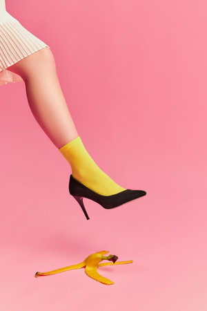 Danger. Creative colorful portrait of female leg in bright yellow socks and banana peel over pink background. Vintage style. Concept of retro fashion, art photography, style, beauty, healthy eatingの写真素材