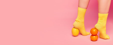 Apple and orange. Banner with female legs in bright yellow socks standing on fruit over pink background. Vintage style. Concept of retro fashion, art photography, style, beauty, healthy eatingの写真素材