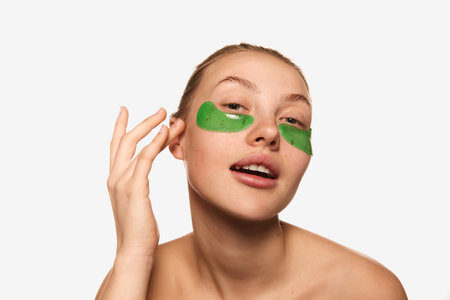 Morning beauty procedure. Closeup young charming girl with bare shoulders using with eye patches for skin refresh. Concept of beauty, natural make-up, skin care, healthy lookの写真素材