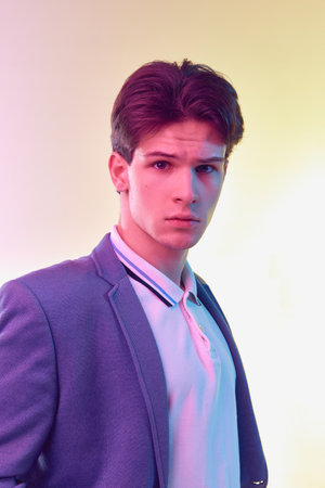 Portrait of young handsome young man, office clerk, student in jacket and jeans posing over light...