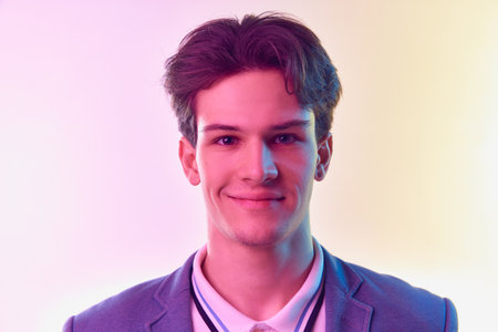 One young Caucasian man, student graduate in jacket posing isolated over light gradient...