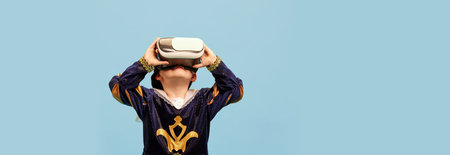 One little boy in costume of medieval pageboy, little prince wearing VR headset standing over blue...