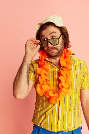Exotic vacation. Man in summer shirt and short with Hawaiian flower garland on chest posing over pink background. Leisure activity, travel, summer, rest and male hobbies conceptの写真素材