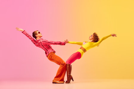Support. Young stylish emotional man and woman, professional dancers in retro style clothes dancing disco dance over pink-yellow background. 1970s, 1980s fashion, music conceptの写真素材