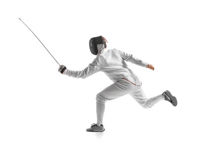 Dynamic portrait of male athlete in fencing costume with sword in hand in action isolated on white...