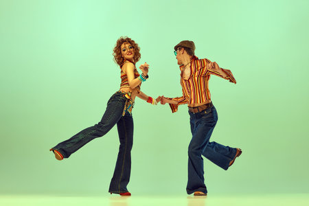 Incendiary dance. Emotional man and woman in retro style clothes dancing disco dance over green background. Concept of fashion trends of 70s, 1980s years, music, hippie lifestyleの写真素材