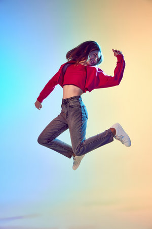 Happiness, relaxation. Happy girl with long hair jumping over pink yellow background in neon light. Concept of human emotions, leisure time, fashion, beauty, adの写真素材