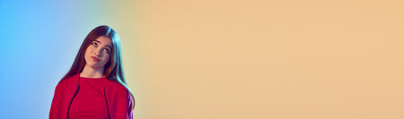 Doubt, challenge. One school pretty girl showing doubt looking away over blue yellow background in neon light. Concept of human emotions, beauty. Banner with copys space for text, adの写真素材