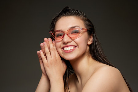 Smiling young woman with well-kept smooth skin looking at camera over grey background. Beauty, skin care, cosmetology, fashion, ad concept. Model looks happy, joyfulの写真素材