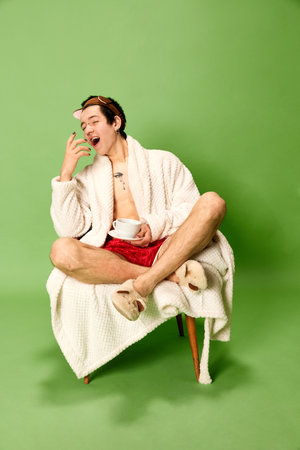 Yawn, sleepy, tired. Portrait of man sitting on chair and want to sleep over green background. Concept of vacation, self love and self care, weekend, rest, relaxの写真素材