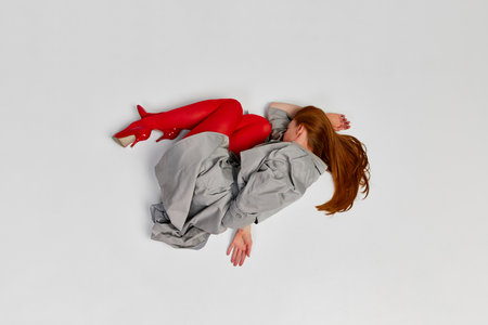 Impersonal human emotions. Stylish girl in grey coat and bright red tights moves over light background. Expressive fashion. Concept of art photography, beauty. Redhaired model in contemporary danceの写真素材