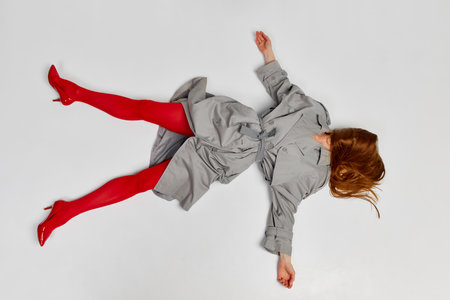 Impersonal human emotions. Stylish girl in grey coat and bright red tights moves over light background. Expressive fashion. Concept of art photography, beauty. Redhaired model in contemporary danceの写真素材