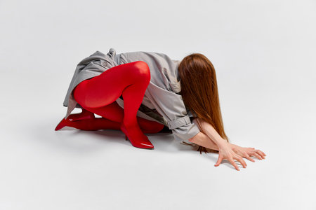Impersonal human emotions. Stylish girl in grey coat and bright red tights moves over light background. Expressive fashion. Concept of art photography, beauty. Redhaired model in contemporary danceの写真素材