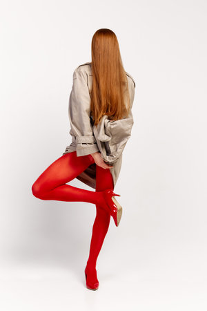 Impersonal human emotions. Stylish girl in grey coat and bright red tights moves over light background. Expressive fashion. Concept of art photography, beauty. Redhaired model in contemporary danceの写真素材