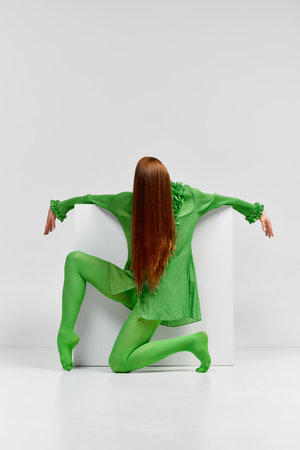 Dance. Avant-garde and experimental art style of human portrait. Unknown woman with long glossy red hair in green outfit posing over light background. Body language, faceless emotions conceptの写真素材
