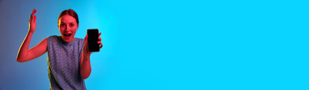 Shocked, breaking news. Banner with excited young pretty girl holding cell phone with empty screen with surprised face. Concept of human emotions, relationship, mood, news, sales. Copy space for adの写真素材