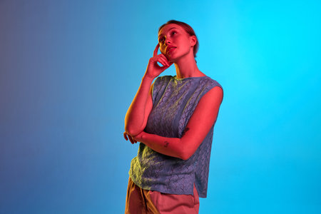 Dreamy, thoughtful, calm. Shot of pensive girl with holded hands standing and thinking about something over blue background in neon light. Concept of beauty, human emotions, mood, adの写真素材