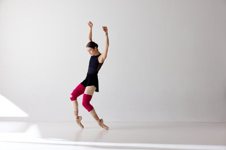 One charming ballerina wearing pointe shoes dancing on fingertips over white background.The art, artist, movement, action and motion concept. Beauty of contemporary danceの写真素材