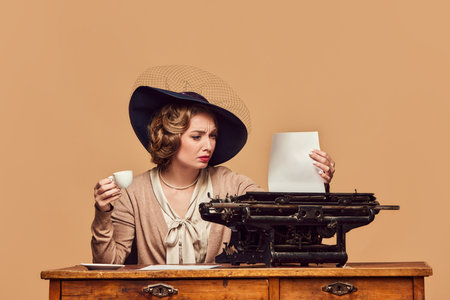 Confused. Attractive woman writer wearing old-fashioned clothes sitting at typewriter with surprised face. Concept human emotions, beauty, fashion, retro style, vintage, 60s, poems, novelの写真素材