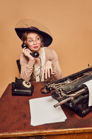 Antipathy. Beautiful woman wearing elegant vintage costume and hat talking on phone with dislike facial expression over beige background Concept emotions, beauty, fashion, retro style, vintageの写真素材