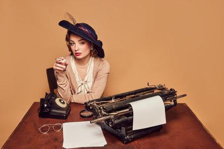Calmness. Attractive woman writer wearing old-fashioned clothes sitting at table and smoking over beige background. Concept poems, novel, emotions, beauty, fashion, retro style, vintageの写真素材