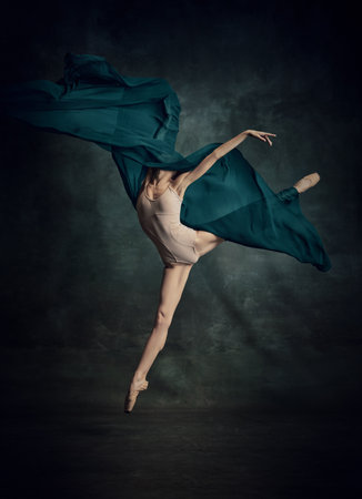Flying with silk. Weightless easy jump. Sensual ballerina with stretched feet dancing with fabric isolated over dark green background. Contemporary dance. Art, inspiration conceptの写真素材