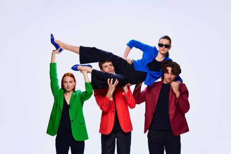 Mutual team support. Group of young workers wearing jackets holding girl over head simbolizing help and trust over white background. Concept of work in team, models, business, online, teleworkingの写真素材