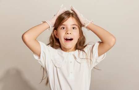 Astonish. Portrait of little pretty girl with long hair wearing white gloves and looking at camera with surprised face. Concept of carefree childhood, holidays, fun, human emotions, facial expressionの写真素材