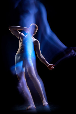 Futuristic man from future. Portrait of young guy wearing underwear in motion over dark background. Mixed neon light. Concept of futurism, surrealism, fashion, cyber, beauty art, adの写真素材