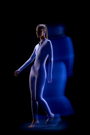 Cyberpunk girl wearing cyber suit walking in motion over dark background. Mixed neon light. Concept of virtual reality, cyberpunk, futurism, surrealism, fashion, cyber, beauty, gesture, art, adの写真素材