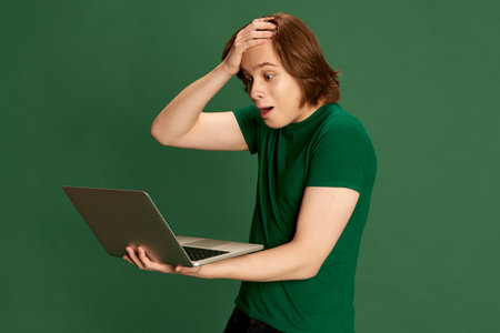 Stressed, astonished. Disappointed salesman trying to understand what happening, holding laptop with questioning facial expression over green background. Concept of business, human emotions, moodの写真素材