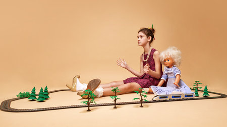 Playing with doll. One little girl wearing dress sitting on floor and clapping her hands over beige background. Vintage, retro, uniqueness, art, childhood, ad, mood, fashion, conceptの写真素材