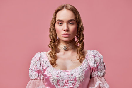 Medieval evil queen. Shot of beautiful princess wearing baroque pink dress and posing on studio background with emotionless face. Concept of medieval, beauty, old-fashioned clothes, human emotions, adの写真素材