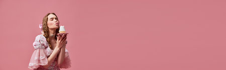 Sweets, sugar addiction. Hungry fairy tale blond princess wearing renaissance dress eating cupcake with satisfaction over pink studio background. Concept of medieval, beauty, food, baroque, adの写真素材