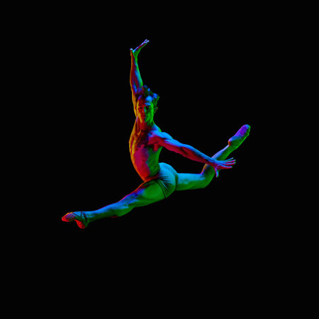 Male twine. Portrait of graceful muscled male ballet dancer jumping up in air over dark studio background with neon light. Grace, art, beauty, contemporary dance concept. Weightless, flexible actorの写真素材