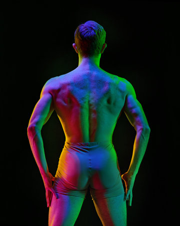 Body in glow. Contemporary art ballet. Young flexible athletic man, dancer posing on dark studio background with neon light. Back view, Modern style dancer. Grace, art, professional sport conceptの写真素材