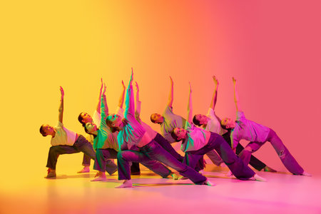 Synchronicity. Group of beautiful teenage girls wearing white t-shirt and jeans dancing together on pink and yellow gradient background in neon light. Modern freestyle dance, contemporary art conceptの写真素材