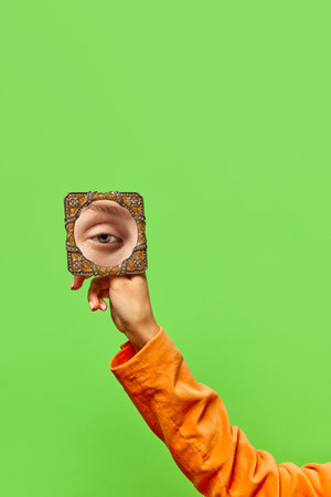 Vintage style. Female hand holding small mirror with reflection of sad girls eye over green background. Concept of vintage fashion, beauty, art, creativity and ad. Human emotions, facial expressionの写真素材