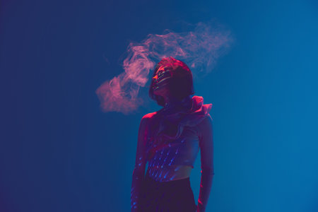 Nicotine addict. Portrait of beautiful sad woman, girl using vape, electronic cigarette over blue background in neon light. Concept of bad habits, emotions, digital art, fashion, cyberpunk, futurismの写真素材
