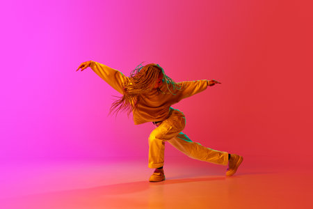 Break dance. Portrait with one young girl, dancer with pigtails dancing with passion over gradient pink background in neon light. Contemporary dance style, motion, art, movement, inspiration conceptの写真素材