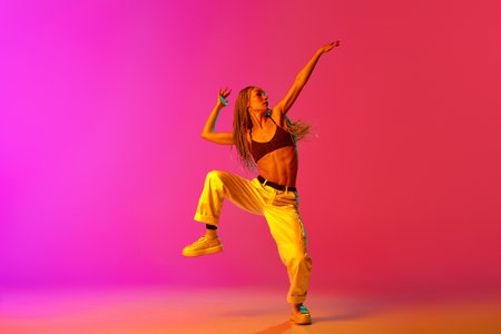 Portrait of young stylish woman, hip-hop dancer training in casual clothes over gradient pink background in neon light. Youth culture, movement, street style, fashion, action, contemporary dance styleの写真素材