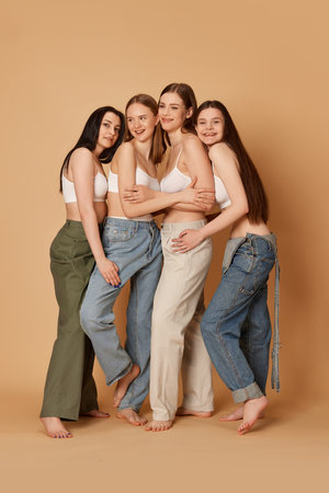 Studio shot with group of young smiling girls wearing casual clothes style posing over beige color background. Concept of natural beauty, body and skin care, healthy eating, fashion, cosmetics, adの写真素材