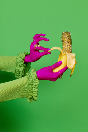 Portrait of colored female hands wearing rings holding gold banana over green studio background. Trash pop art, bright colors. Concept of meal, jewelry, fruits, diet, fashion, beauty, sales, adの写真素材