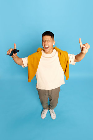 Portrait with excited young man, guy, student in stylish casual clothes listening to music via...