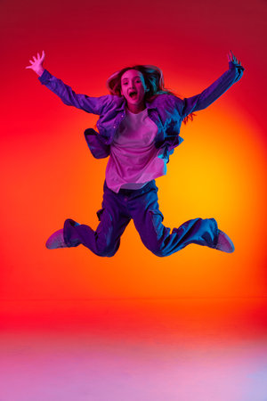 Freedom. Funny portrait of emotive, young girl wearing casual clothes levitating in air over red color studio background in neon light. Concept of beauty, youth, human emotions, dreams, student lifeの写真素材