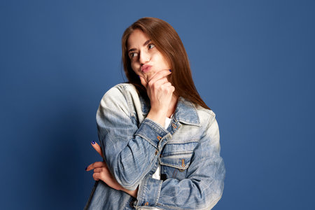 Portrait of funny, pensive girl wearing casual style clothes grimacing with doubtful face over blue color studio background. Concept of happiness, human emotions, fashion, beauty, youth, fun, adの写真素材