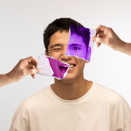 Human hands holding photo parts of young asian mans face with different emotions. Happiness and anger. Conceptual art collage. Concept of human emotions, diversity, inner world, psychologyの写真素材