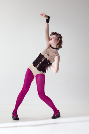 Extraordinary look. Portrait of pretty young girl in black corset and pink tights with blushing cheeks posing over grey studio background. Concept of female beauty, art, femininity, fashion, emotionsの写真素材