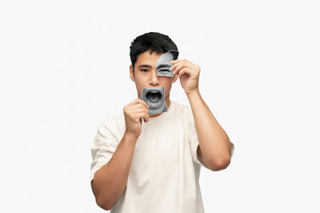 Young asian man with calm face holding photo face parts expressing anger and irritation. Creative...